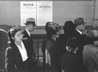 Figure 27.14 Japanese Americans standing in line in front of a poster detailing internment orders in California.
